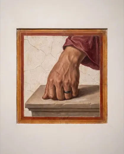 Primer plano de una mano con un anillo de hierro apoyada sobre piedra.